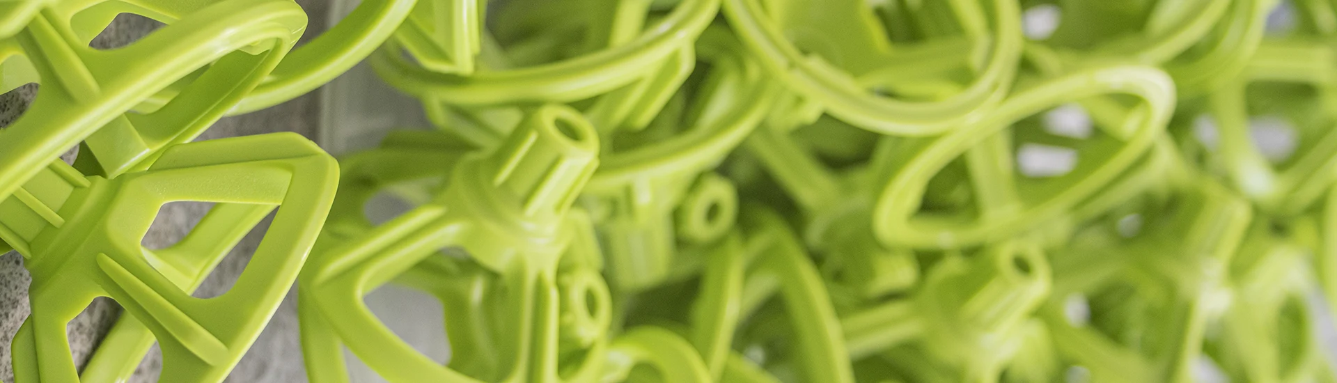 A collection of green tile leveling devices piled on a gray surface, with the nearest ones in sharp focus and the rest fading into a blur.